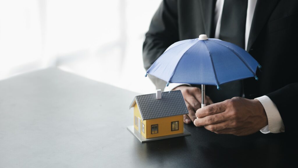 Individuals holding small umbrellas and model homes, housing insurance against impending loss and fi